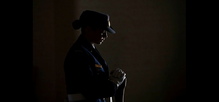 A female officer in uniform holds a baton, creating a striking silhouette.